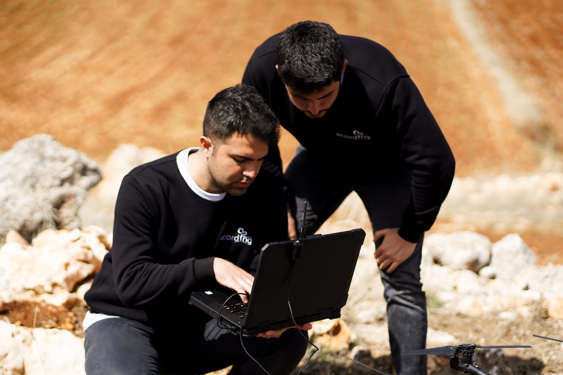 Açık havada dayanıklı bir bilgisayarda çalışan iki ekip üyesi, yanlarında yerde duran bir ecoDrone