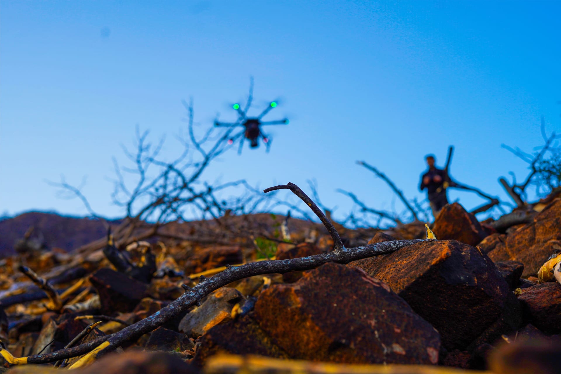A survey drone flying over burnt ground where blackened branches remain